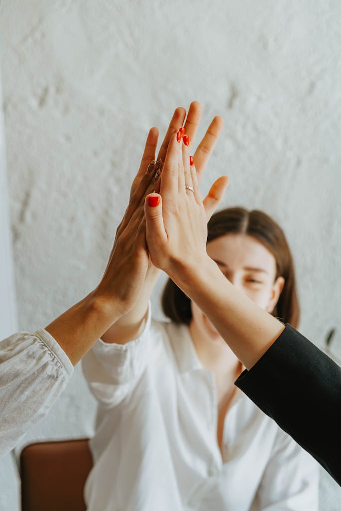 Photo by olia danilevich A group of adults in a warm atmosphere celebrating teamwork with a high-five gesture.