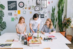 Art class scene with students and instructor working on creative projects in a bright, indoor studio.