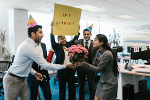 Happy office birthday celebration with colleagues exchanging gifts and wearing party hats.