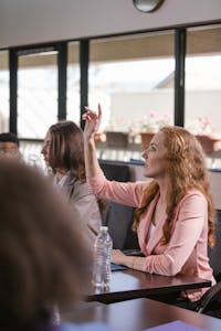 Red-haired woman actively participating in a business meeting, raising hand for discussion.