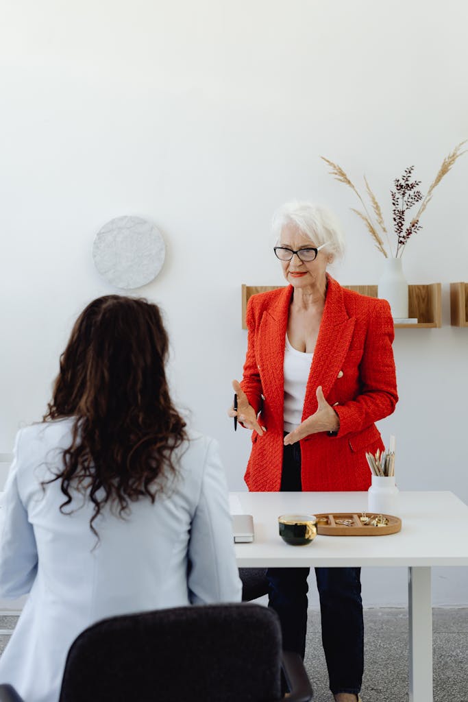 Senior woman in red blazer presenting during a business meeting in a modern office.