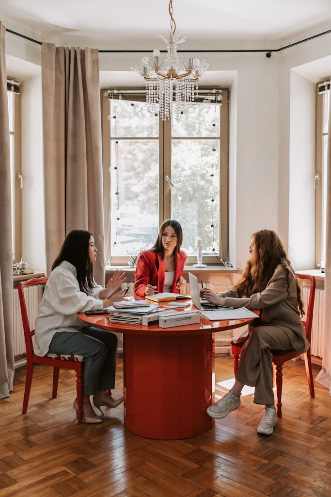 Three women engaged in a business meeting around a table in a stylish office setting.