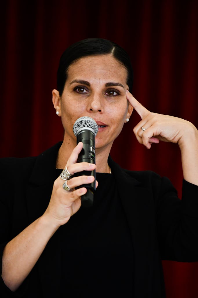 Woman in black suit delivering a speech holding a microphone indoors.