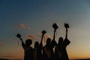 A group of graduates celebrate by raising their caps against a vibrant sunset sky, symbolizing achievement.