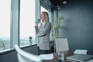 A professional businesswoman enjoys a cup of coffee while overlooking a cityscape from her modern office window.