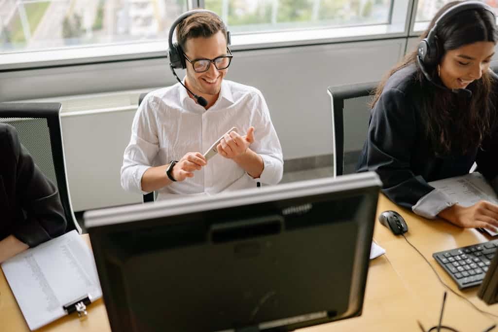 Colleagues working at a desk with computers and headsets in a modern office setting.