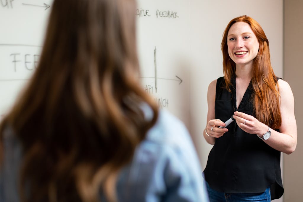 Two women discussing and planning a project in an office setting using a whiteboard.