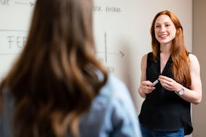 Two women discussing and planning a project in an office setting using a whiteboard.